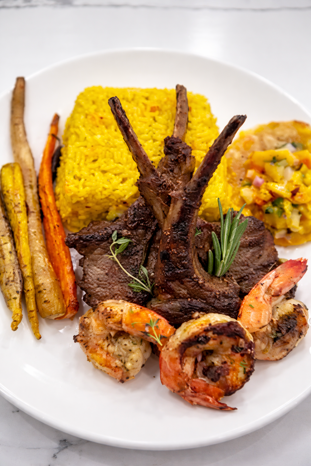 Plated dish with lamb chops, shrimp, carrots, and yellow rice on a white plate.
