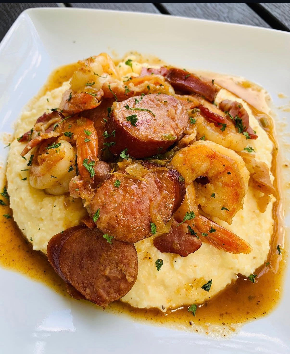 Platter of shrimp and sausage over creamy grits on a white plate.