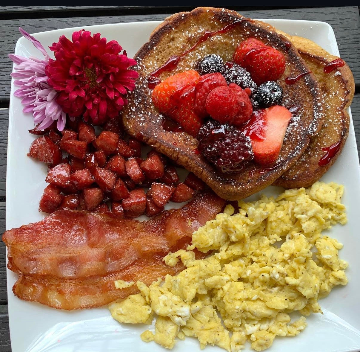 Breakfast plate with pancakes, berries, bacon, and eggs on a white plate.