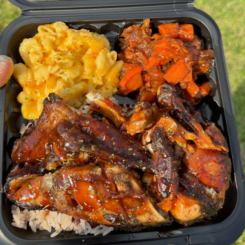 Takeout container with ribs, macaroni and cheese, and rice on a grassy background